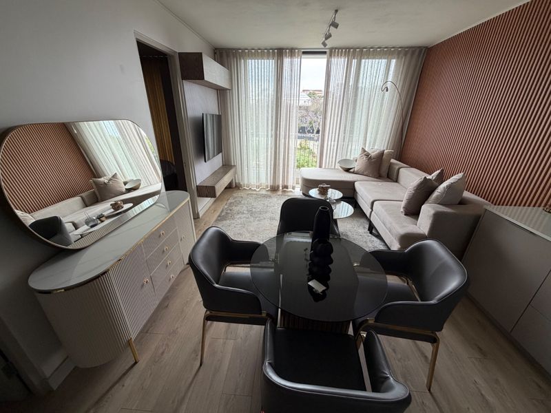 Modern open-plan living and dining area featuring stylish slatted wall paneling, laminate flooring, and a built-in media console with access to a balcony.
