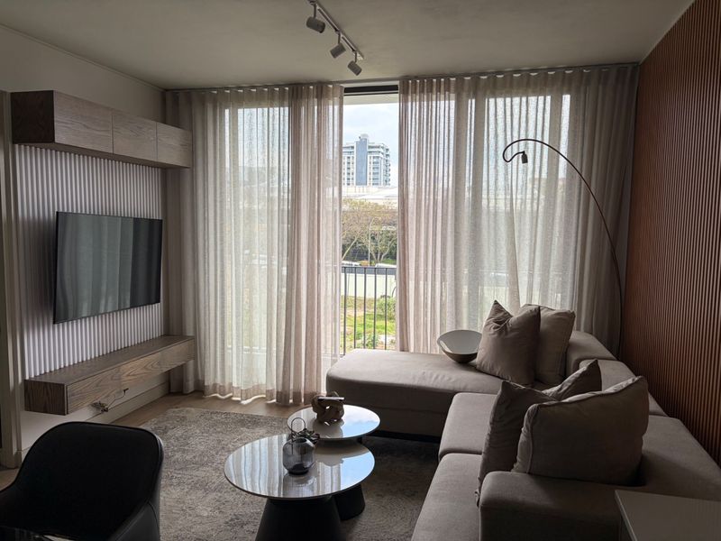 Modern living room featuring elegant slatted wall paneling, built-in media cabinetry, track lighting, and large sliding doors leading to a balcony with city views.