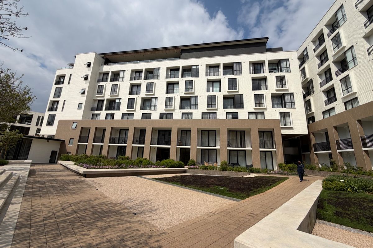 A modern multi-story apartment complex featuring a well-maintained paved courtyard, landscaped garden beds, and private balconies for residents.