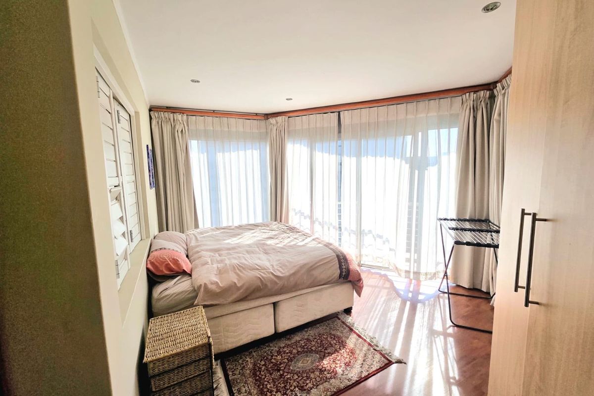 A bright bedroom featuring laminate flooring, built-in wardrobe storage, and large windows with curtains allowing for ample natural light.