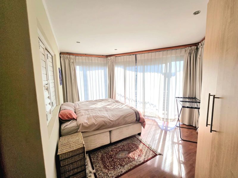 A bright bedroom featuring laminate flooring, built-in wardrobe storage, and large windows with curtains allowing for ample natural light.