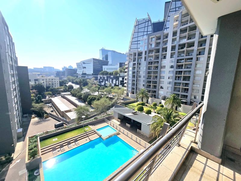 Elevated urban view overlooking a residential complex with a swimming pool, landscaped gardens, and surrounding city architecture.