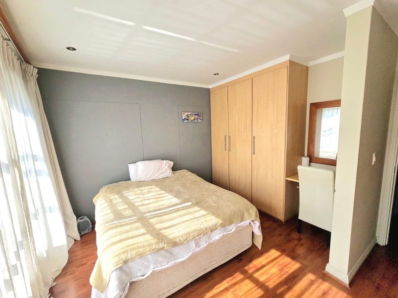 A well-lit bedroom featuring laminate flooring, built-in wooden cupboards, and a convenient integrated vanity area.