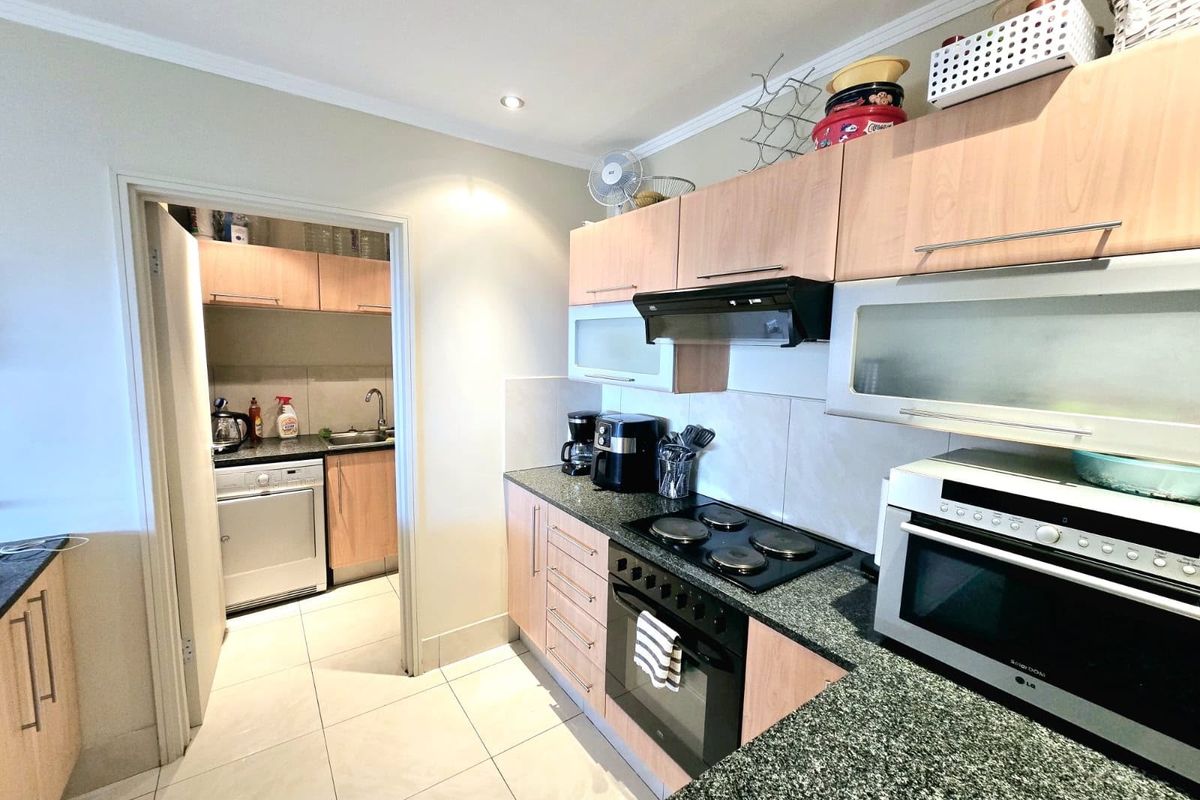 Functional kitchen featuring laminate cabinetry, granite countertops, and integrated appliances, with an adjoining scullery area and tiled flooring throughout.