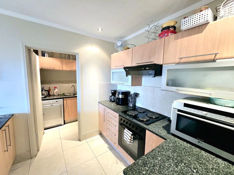Functional kitchen featuring laminate cabinetry, granite countertops, and integrated appliances, with an adjoining scullery area and tiled flooring throughout.