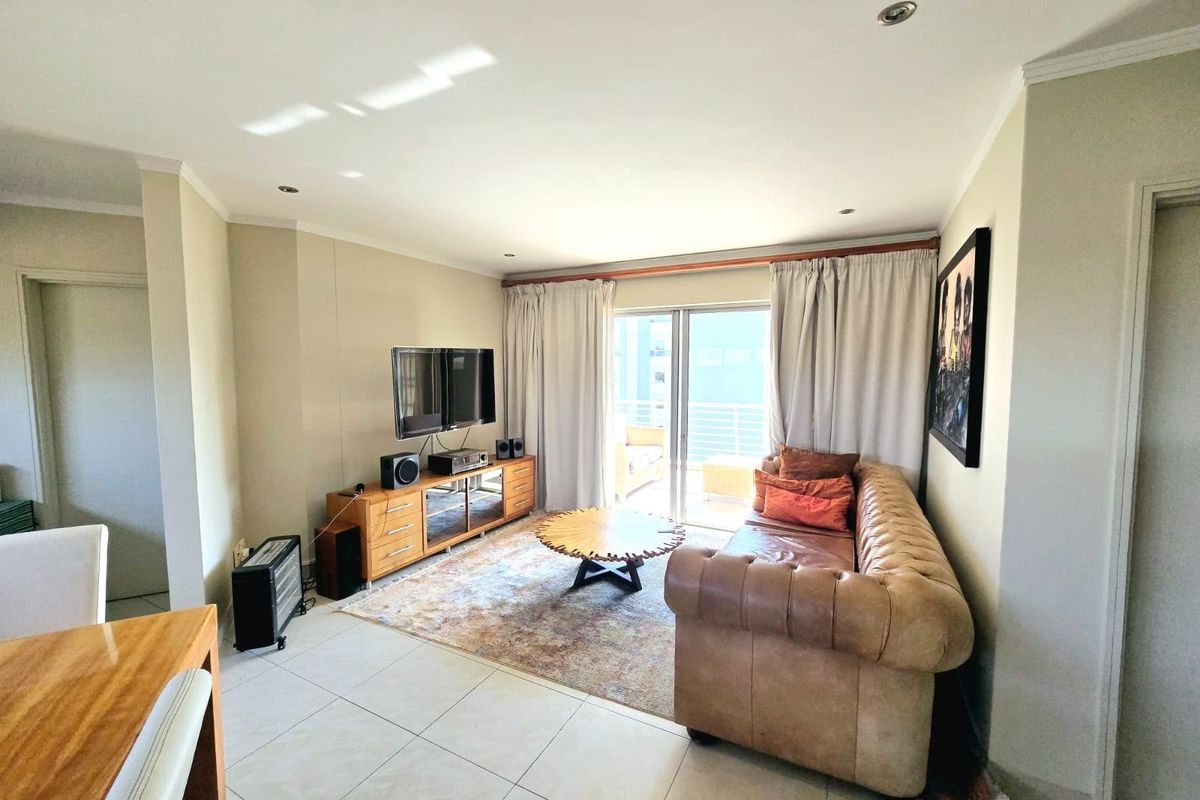 A bright and spacious living room featuring tiled flooring, recessed downlighting, and large sliding glass doors that provide access to the balcony.