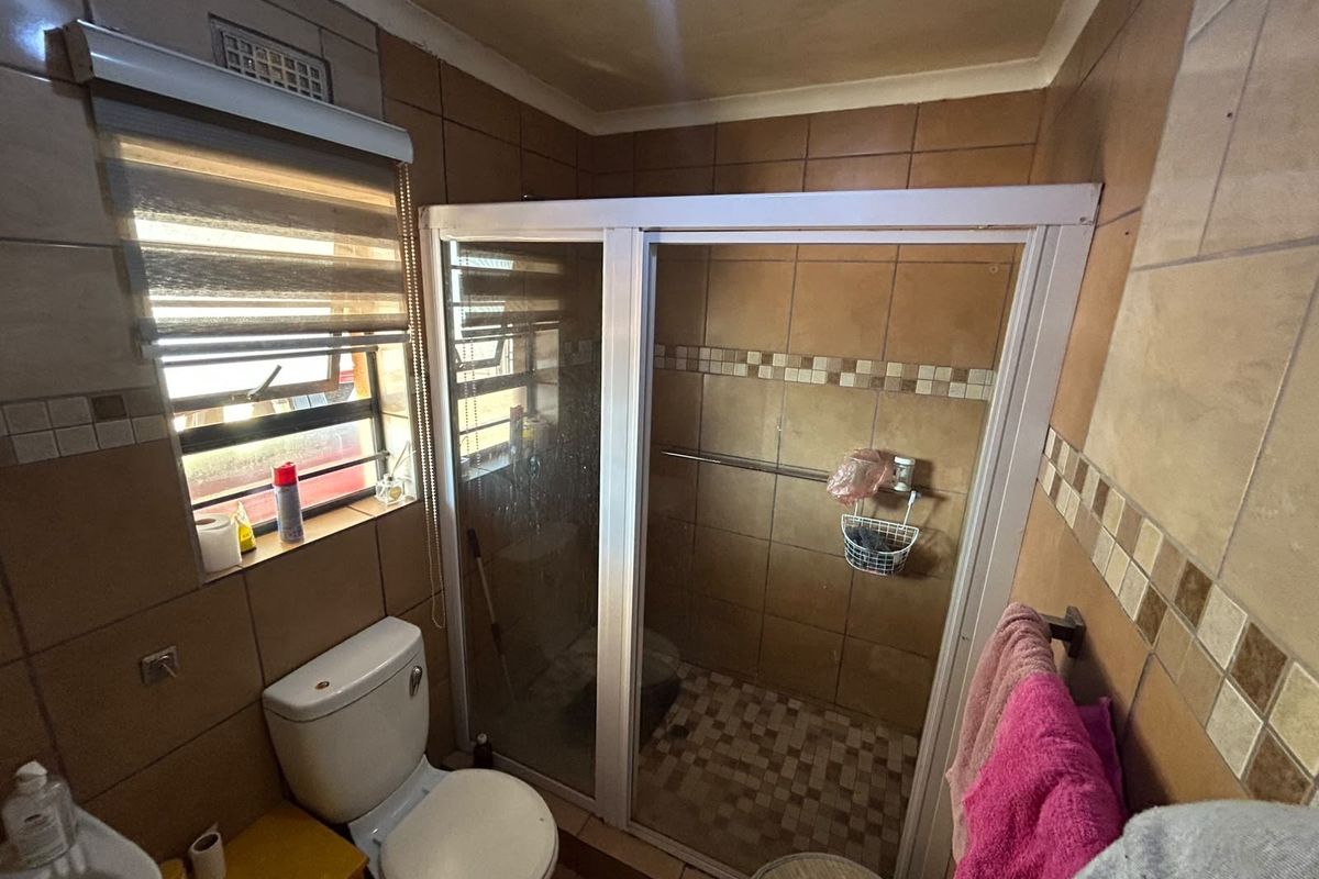 A compact bathroom featuring a shower enclosure, toilet, and washbasin with dated brown wall tiling and a tiled floor.