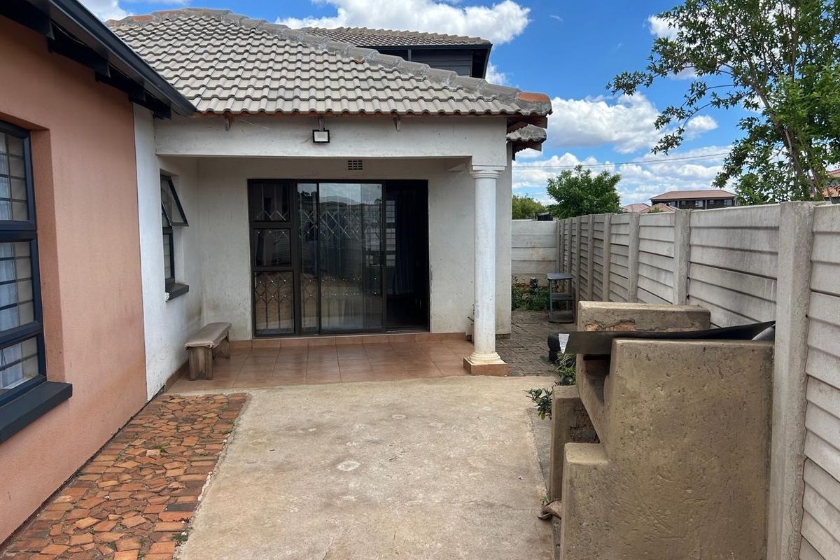 Rear exterior view featuring a covered patio, built-in concrete braai, and a precast concrete boundary wall.