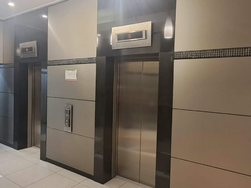 Modern office building lobby featuring stainless steel elevator banks, sleek metal wall paneling, and integrated mailboxes with polished tile flooring.