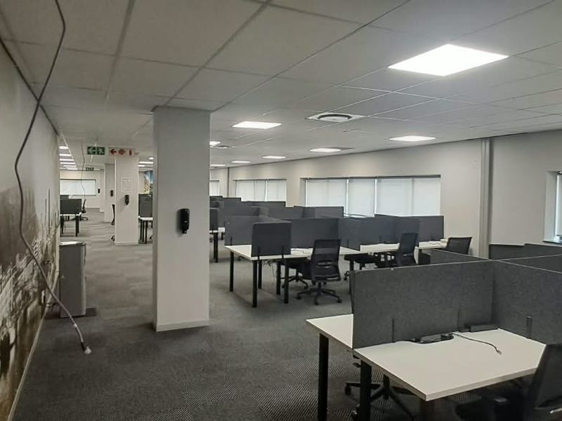 Open-plan office space featuring a suspended ceiling with recessed lighting, carpeted flooring, and multiple workstation cubicles with integrated privacy screens.