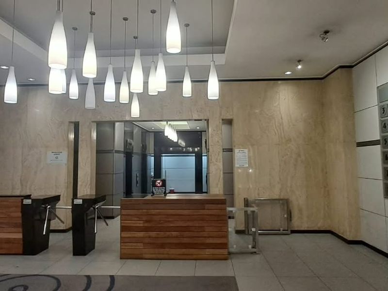 Professional office building entrance lobby featuring marble wall cladding, a reception desk, security turnstiles, and modern pendant lighting.