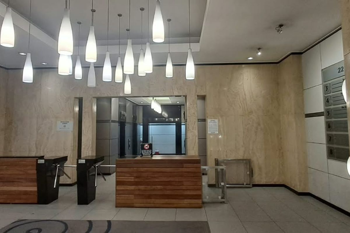 Professional office building entrance lobby featuring marble wall cladding, a reception desk, security turnstiles, and modern pendant lighting.