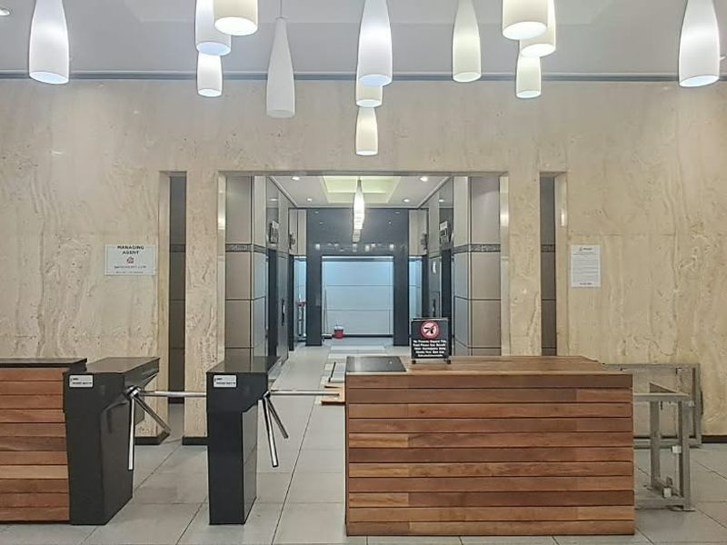 Professional office building lobby featuring marble wall finishes, a reception desk, secure turnstile access, and modern pendant lighting leading to the elevator bank.
