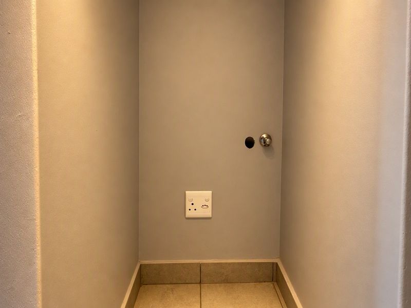 A small utility alcove featuring tiled flooring and an electrical outlet, currently showing a missing door handle and an exposed hole in the wall.