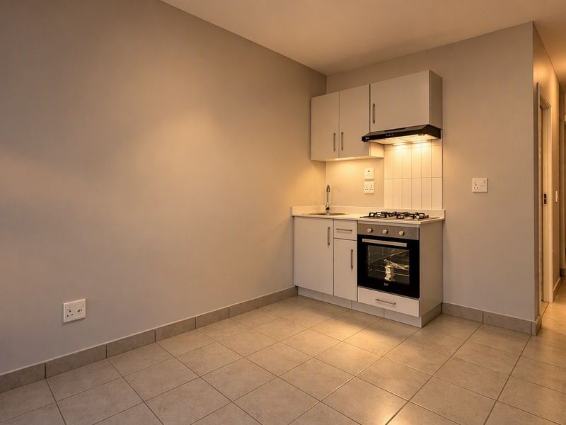 Compact kitchen area featuring built-in cabinetry, gas hob, oven, extractor fan, and tiled flooring in a clean, modern apartment setting.