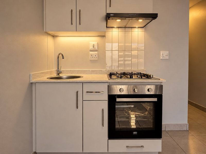 A compact, modern kitchen featuring white cabinetry, stone countertops, a gas hob, built-in oven, and integrated extractor fan with under-cabinet lighting.