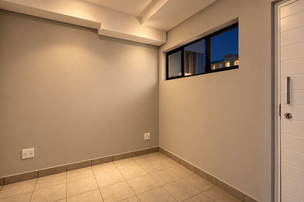 A clean, empty bedroom featuring neutral wall tones, tiled flooring, a built-in cupboard, and a horizontal window providing natural light.
