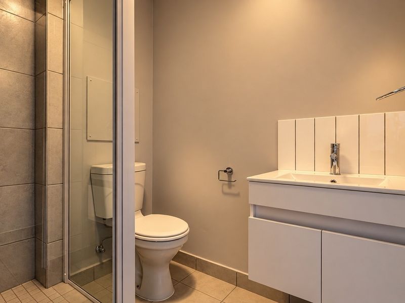 A clean and modern bathroom featuring a glass-enclosed shower, a white vanity with basin, and neutral wall and floor tiling.