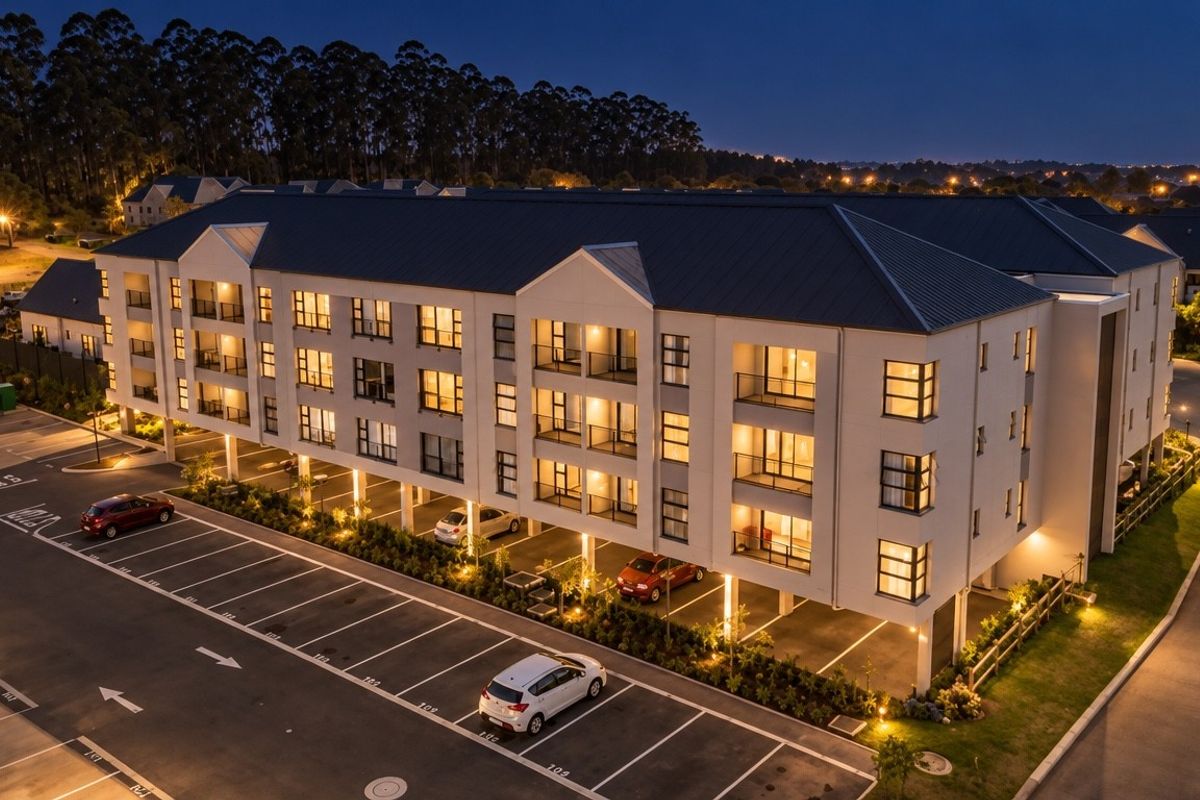 Aerial view of a modern multi-story apartment complex at dusk, featuring covered parking, balconies, and well-maintained exterior landscaping.