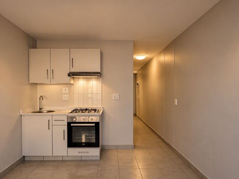 Compact kitchen featuring white cabinetry, built-in oven, gas hob, extractor fan, and tiled splashback, leading into a tiled hallway.