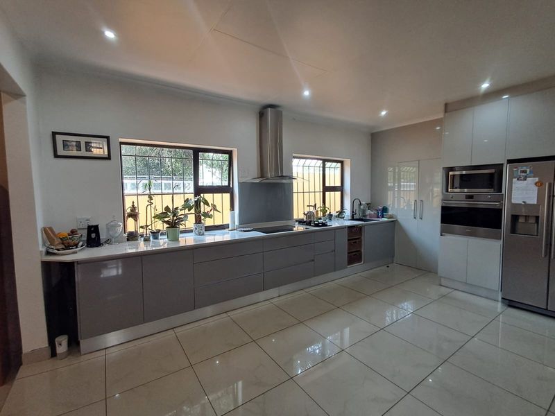Modern kitchen featuring sleek grey cabinetry, stone countertops, integrated stainless steel appliances, and polished tiled flooring with ample natural light.