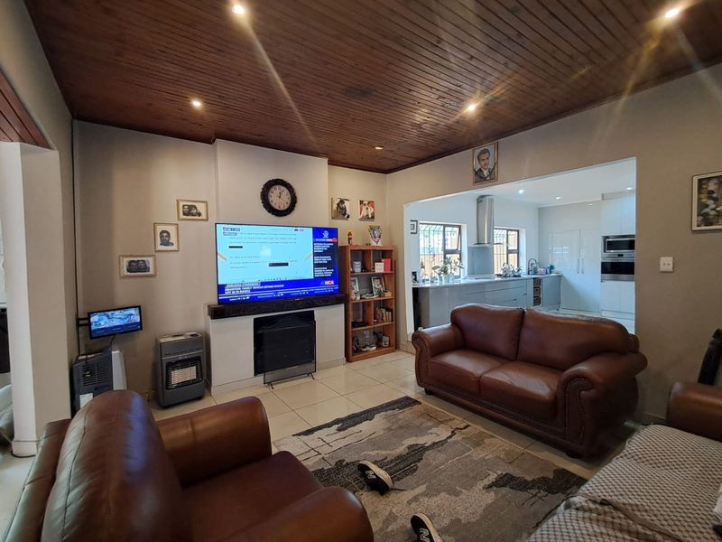 Open plan living area featuring a timber ceiling, tiled floors, and a built-in fireplace, flowing into a modern kitchen with integrated appliances.