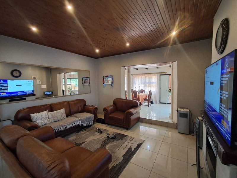 Spacious living room featuring a warm timber ceiling, recessed lighting, and tiled flooring, with an open-plan flow leading into the adjacent dining area.