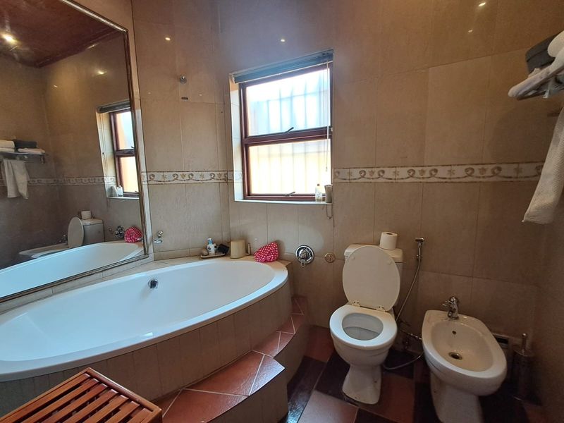 A functional bathroom featuring a built-in bathtub, toilet, bidet, and tiled finishes, complemented by a large wall mirror and natural light from the window.