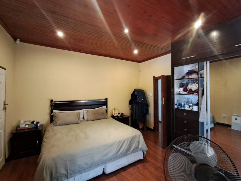 A bedroom featuring a timber ceiling, laminate flooring, and a built-in wardrobe with mirrored sliding doors.