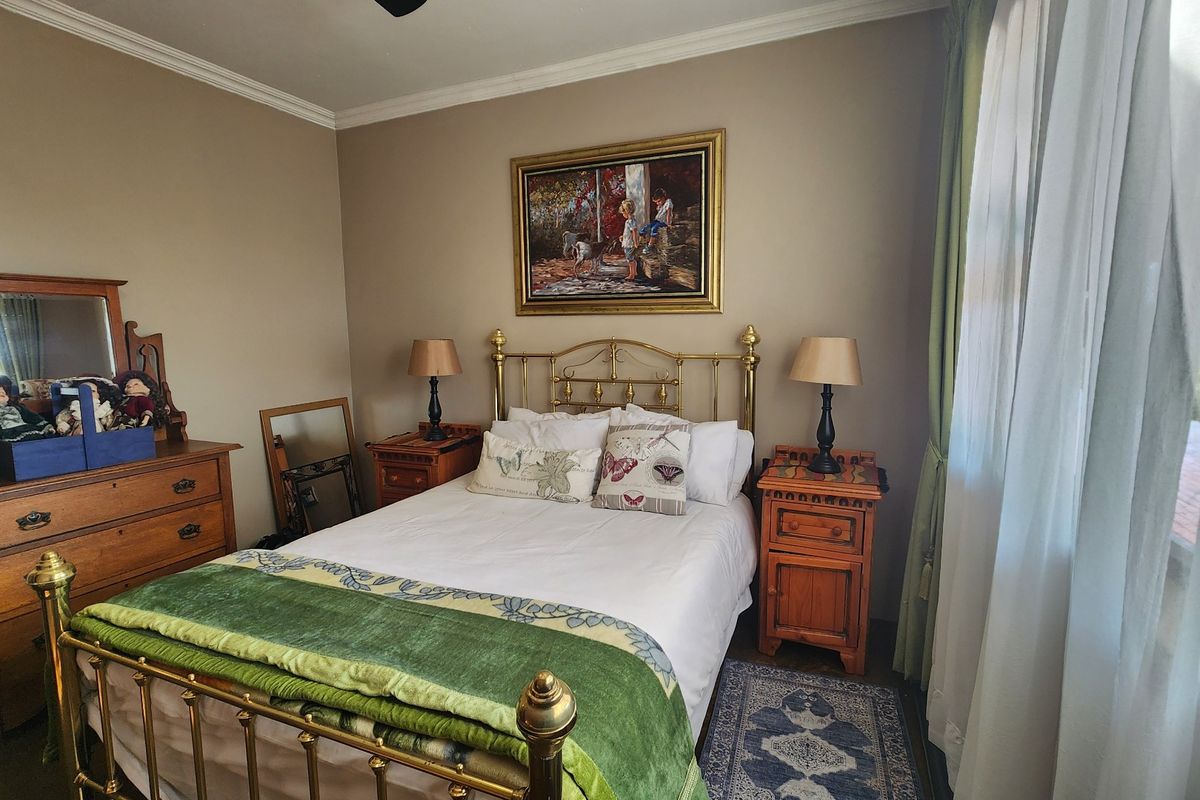 A cozy bedroom featuring neutral wall tones, crown molding, and large windows with curtains, providing a comfortable and well-maintained living space.