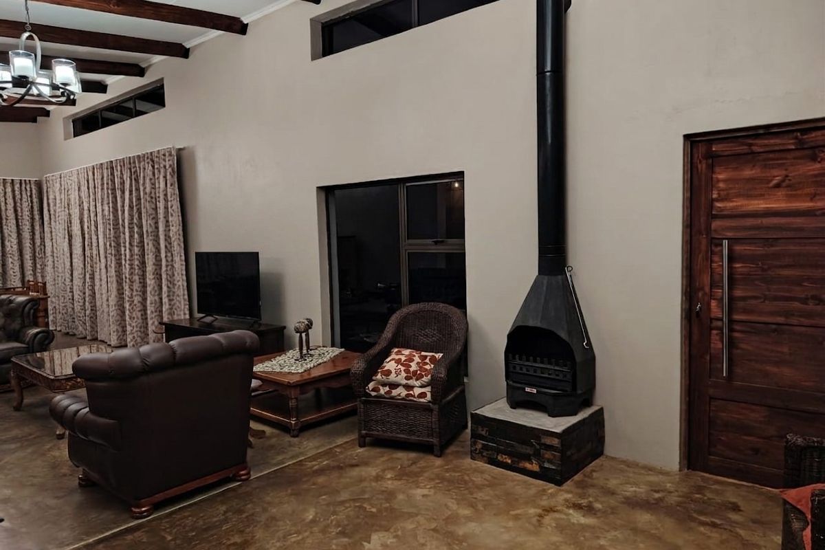 Spacious living room featuring polished concrete floors, exposed timber ceiling beams, a modern freestanding fireplace, and clerestory windows for natural light.