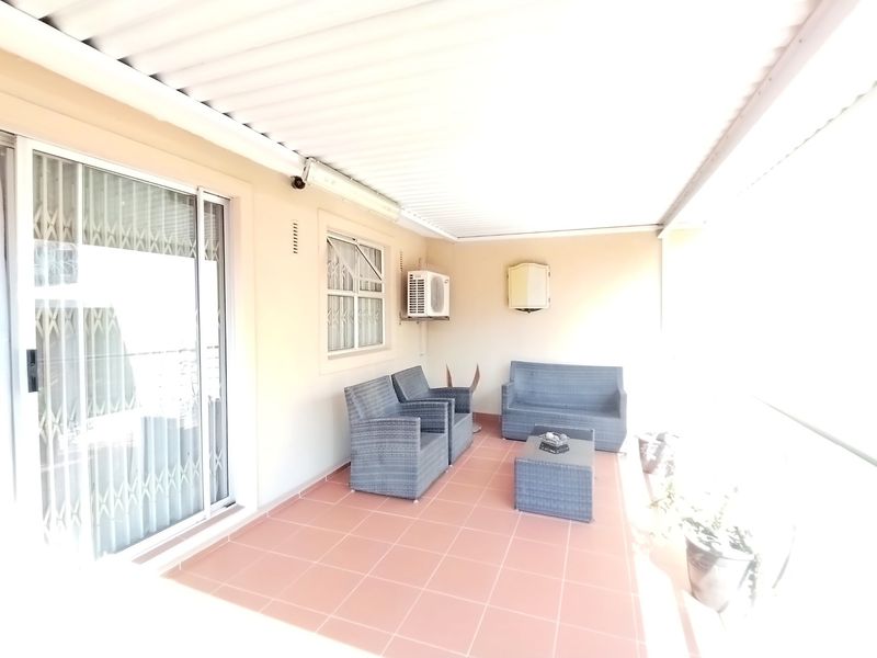 A covered patio area featuring tiled flooring, a sliding glass door with security gate, and a wall-mounted air conditioning unit.