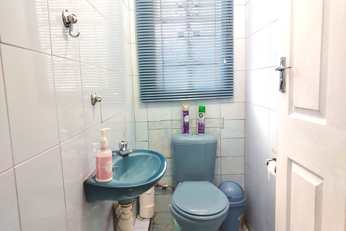 A compact bathroom featuring a blue wall-mounted basin and matching toilet, finished with light-colored wall tiles and a window blind.