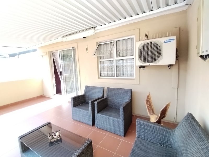 A covered patio area featuring tiled flooring, a sliding door entrance, and an external air conditioning unit mounted on the wall.