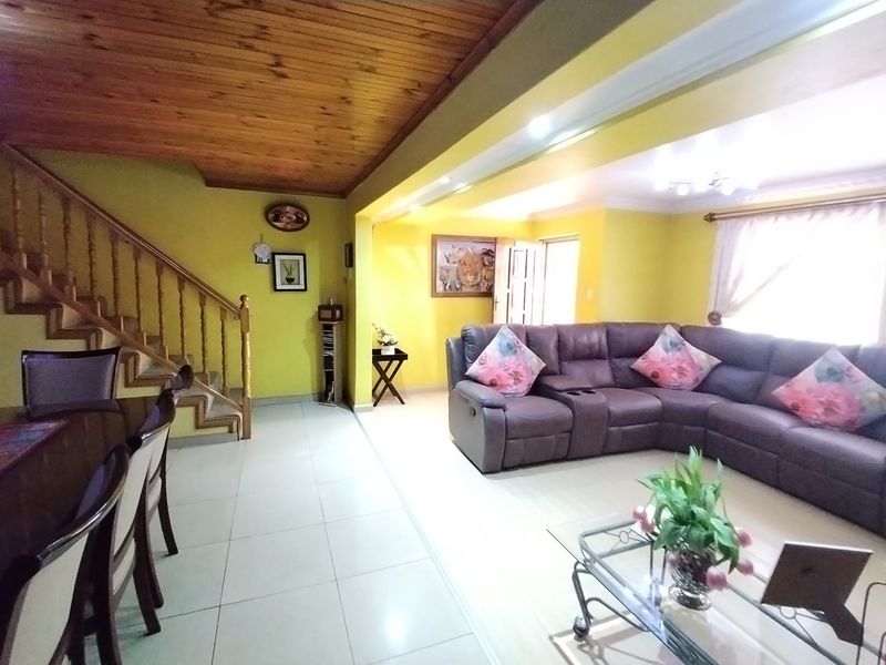 Spacious open-plan living area featuring tiled flooring, a wooden staircase, and a distinctive wooden ceiling with recessed lighting.