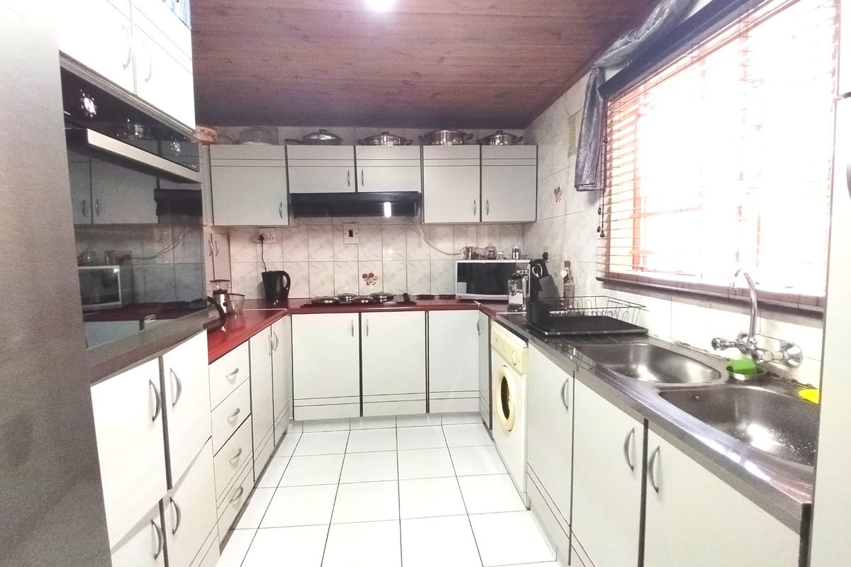 A functional kitchen featuring built-in cabinetry, a double bowl stainless steel sink, integrated oven, hob, and extractor fan with tiled finishes.