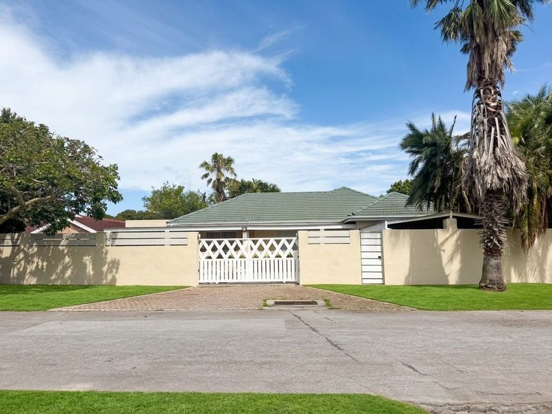 Front view of the property featuring a secure perimeter wall, paved driveway, and gated entrance with a tiled roof house visible in the background.