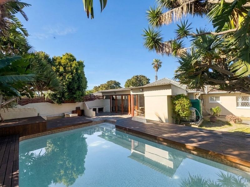 Outdoor pool area featuring timber decking, a built-in braai, and a water tank, set within a private garden space.