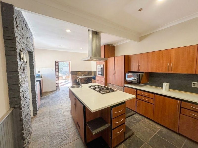 Spacious kitchen featuring a central island with gas hob, extractor fan, stone countertops, and ample built-in cabinetry with direct access to the outdoor area.