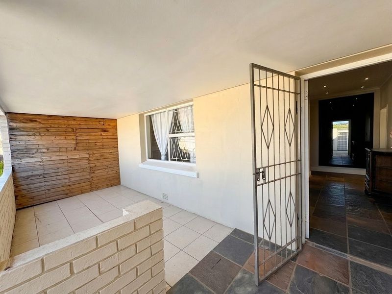 A covered patio area featuring tiled flooring, timber wall cladding, and a brick half-wall, providing a functional outdoor space with security gate access.