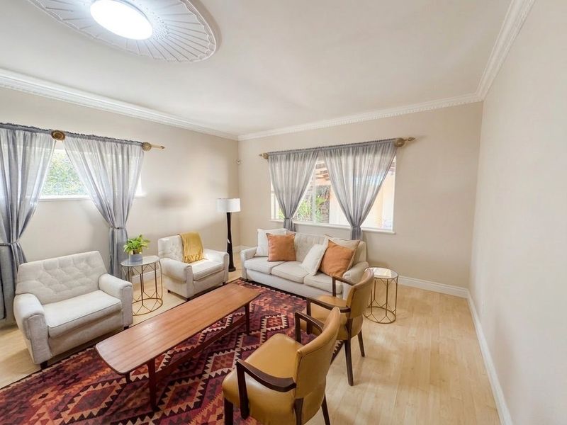 A bright and well-maintained living room featuring crown molding, a decorative ceiling rose, and light-toned laminate flooring.