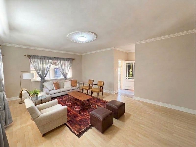 A spacious and well-lit living room featuring light laminate flooring, decorative ceiling rose, and classic coving, providing a comfortable and inviting atmosphere.