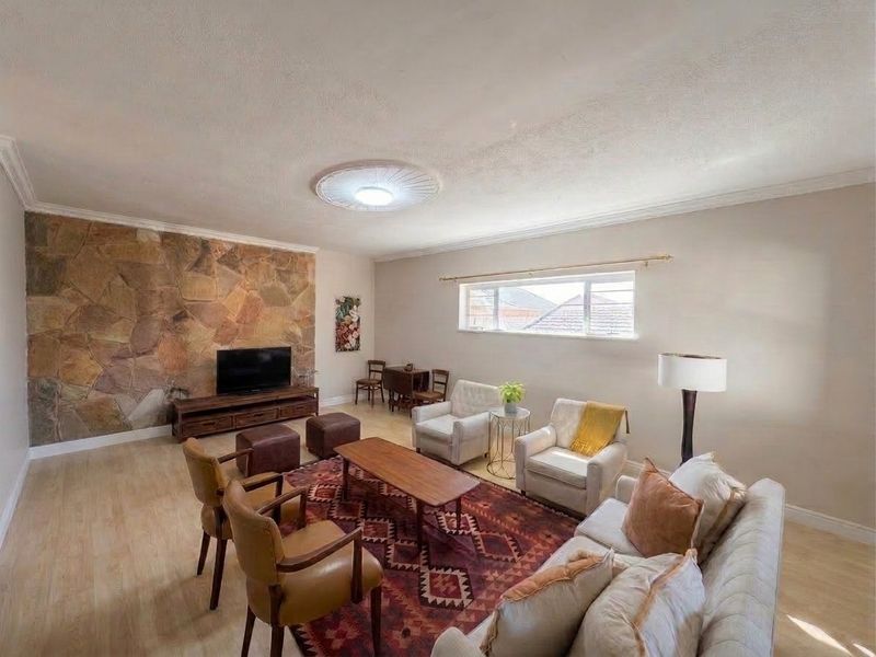 Spacious living room featuring a prominent stone accent wall, laminate flooring, and decorative ceiling rose, offering a comfortable and well-lit living space.