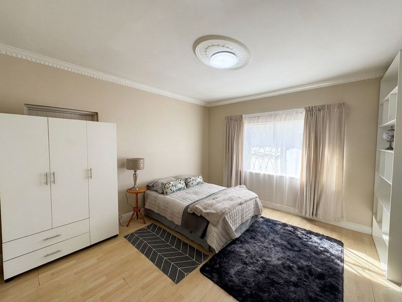 A well-maintained bedroom featuring laminate flooring, decorative crown molding, a ceiling rose, and built-in shelving units.