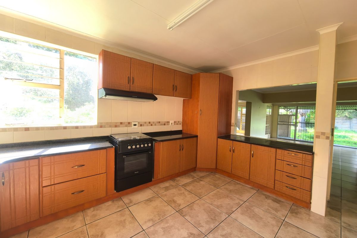 A functional kitchen featuring wood-look cabinetry, black countertops, built-in oven with extractor, and tiled flooring, with a convenient pass-through window to the adjacent living area.