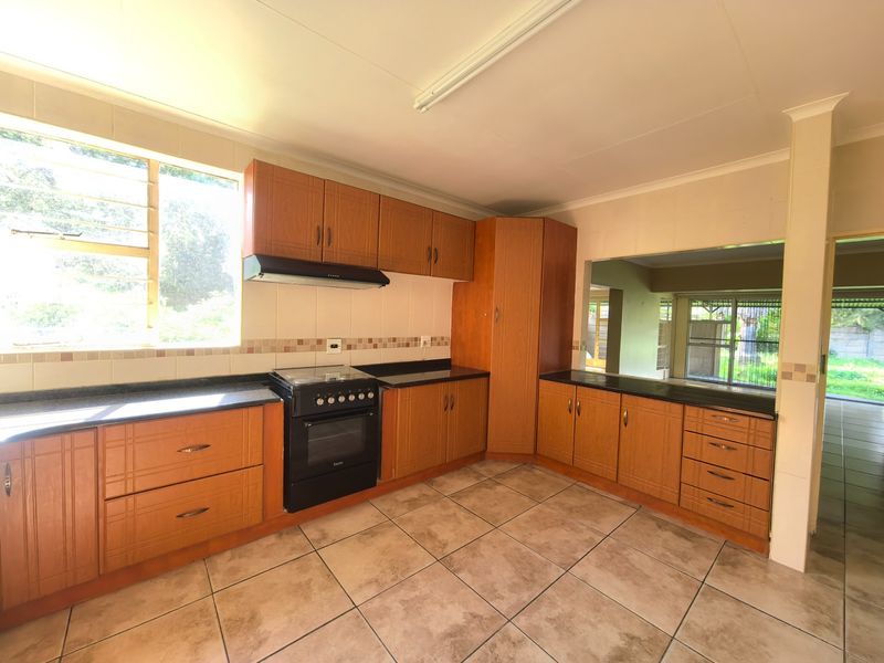 A functional kitchen featuring wood-look cabinetry, black countertops, built-in oven with extractor, and tiled flooring, with a convenient pass-through window to the adjacent living area.