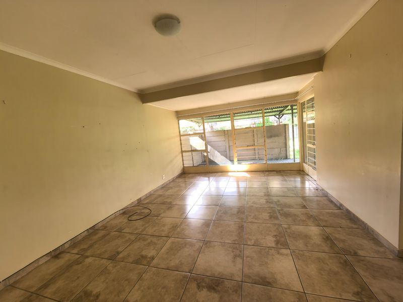 An empty, spacious living area featuring neutral tiled flooring and large glass doors that provide ample natural light and access to the exterior.