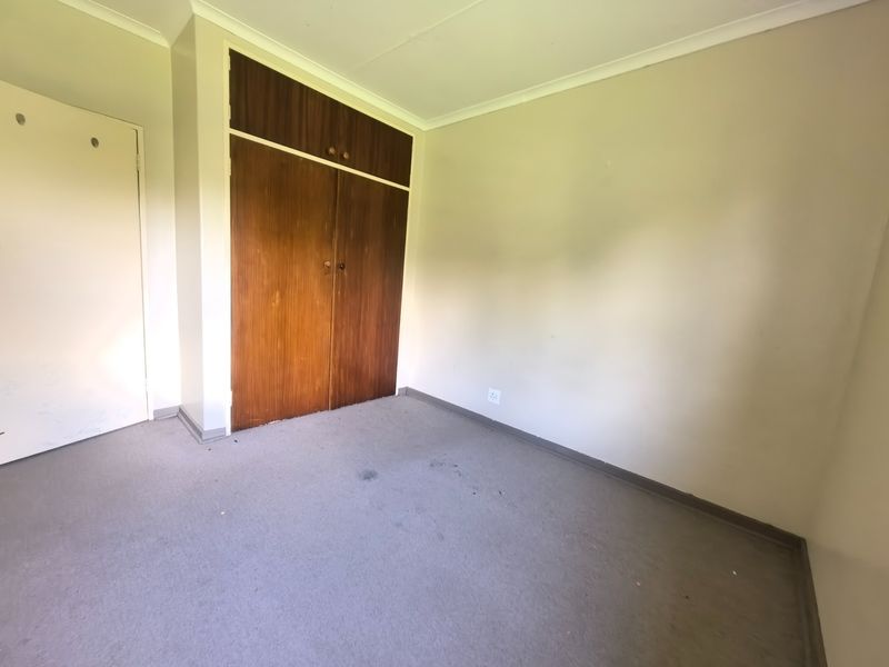 An empty bedroom featuring built-in wooden wardrobes, neutral wall finishes, and carpet flooring, offering a blank canvas for potential updates or staging.