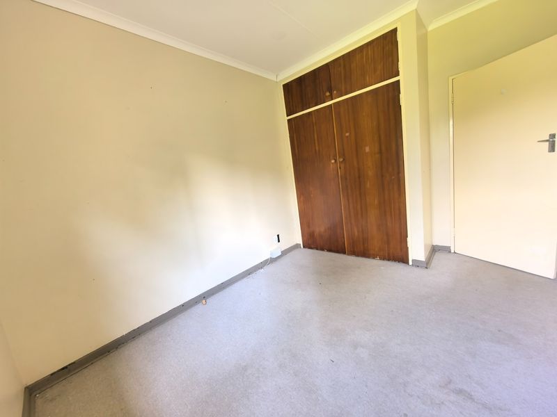 An empty bedroom featuring built-in wooden cupboards, neutral wall paint, and carpeted flooring, offering a blank canvas for renovation or staging.