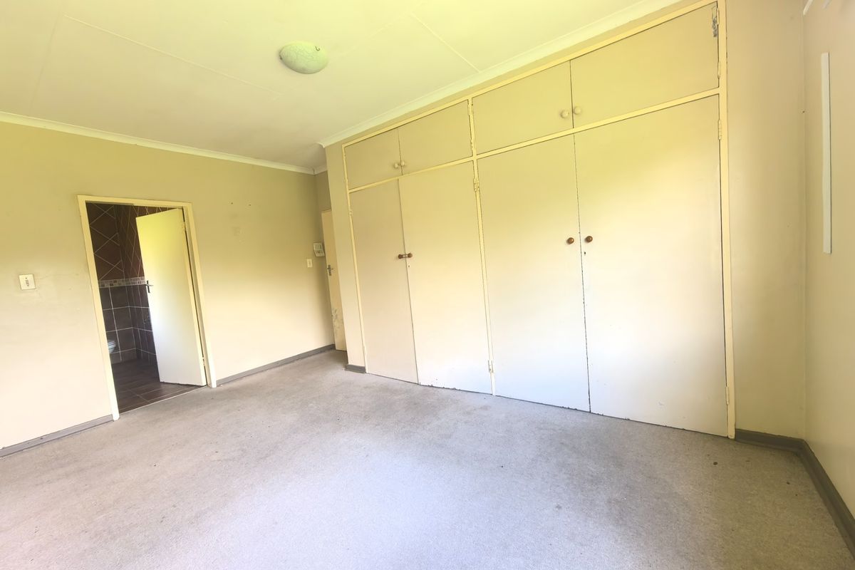 An empty bedroom featuring built-in cupboards, carpeted flooring, and direct access to an en-suite bathroom.